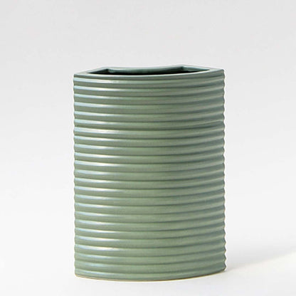 Closeup of green ceramic vase showcasing ribbed lines and smooth matte finish with arrangement in natural light.