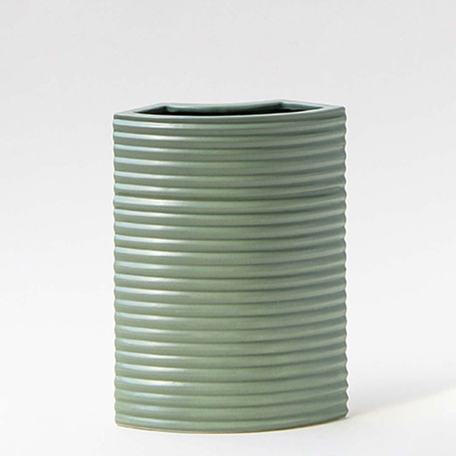 Closeup of green ceramic vase showcasing ribbed lines and smooth matte finish with arrangement in natural light.