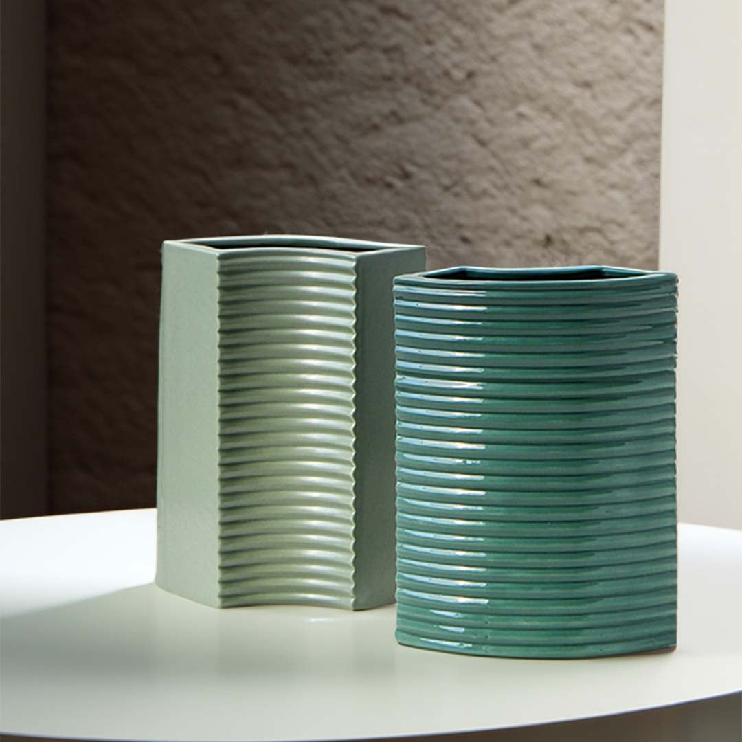 Collection of ribbed green ceramic vases arranged with white flowers on wooden surfaces for a refined modern decor theme.