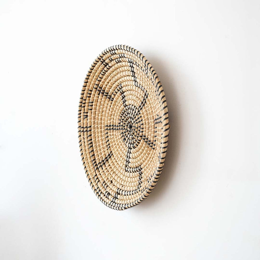 Side view of handwoven wall basket decor made of rustic natural fiber with black swirl design for boho wall styling.