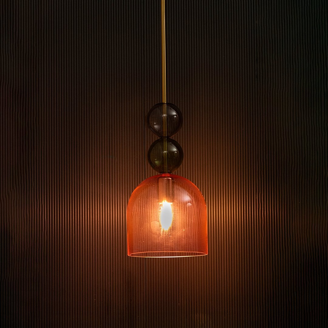 Artistic pink glass pendant light illuminated beautifully on dark background highlighting its sculptural elegance.