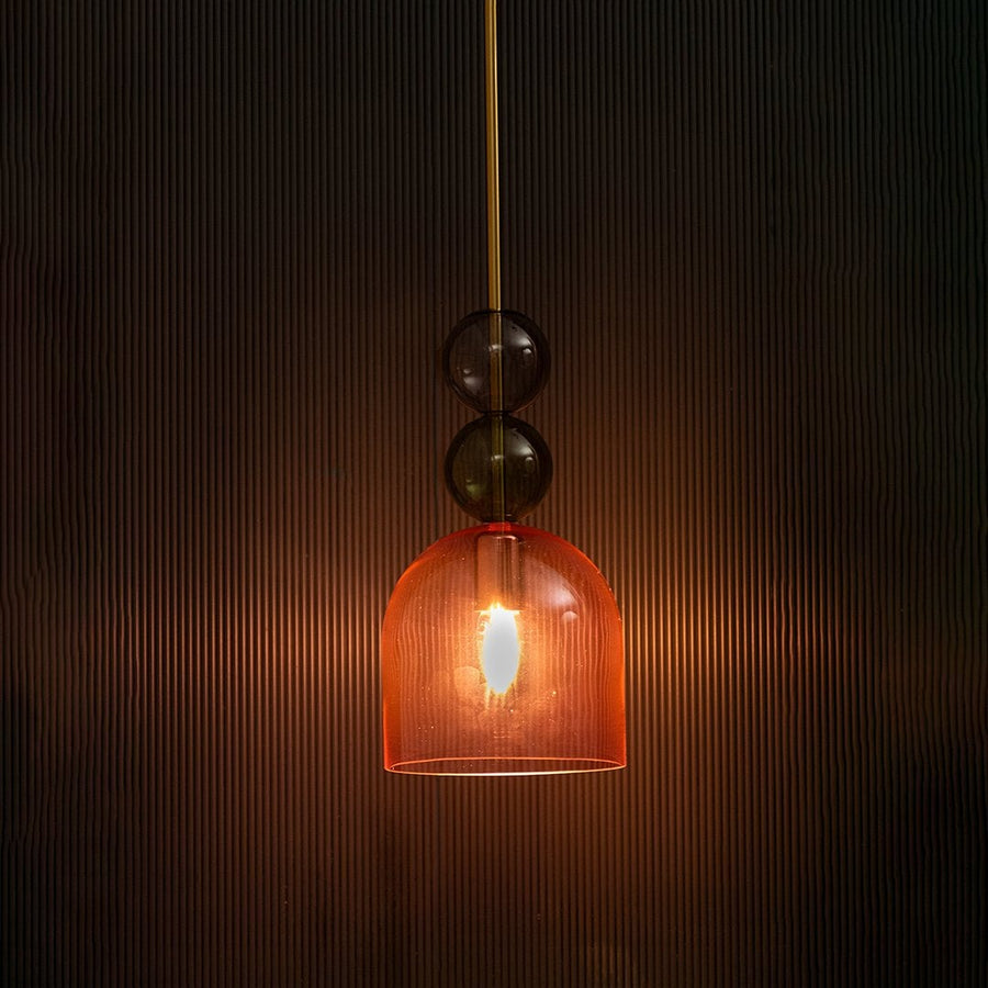 Artistic pink glass pendant light illuminated beautifully on dark background highlighting its sculptural elegance.