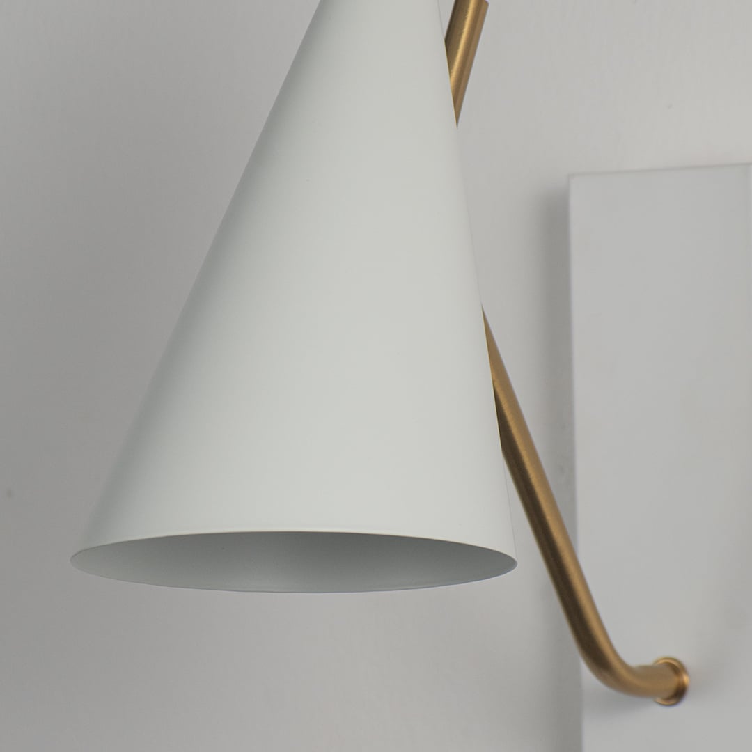 Elegant wall light with matte white conical shade and slim gold arm in closeup view highlighting minimal contemporary design.
