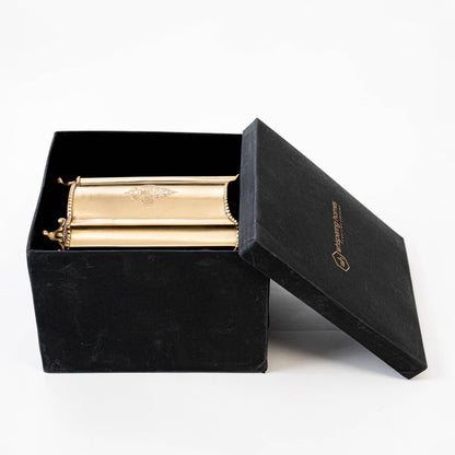 Cylindrical gold brass container neatly packed in premium black gift box with open lid placed on white surface.