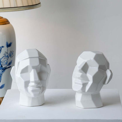 Contemporary geometric face sculpture arranged in a styled setting on a white block  emphasizing form  shadows  and artistic character.