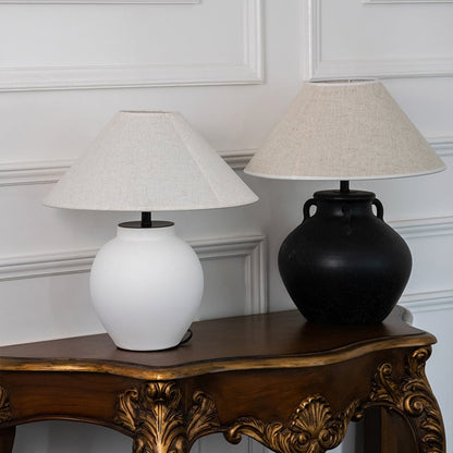 White ceramic table lamp with fabric shade displayed on a carved wooden console table offering warm classic decor lighting.