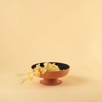 Terracotta textured metal pedestal bowl with black interior styled in a warm neutral scene adding earthy modern charm to decor.