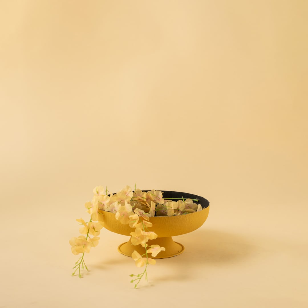 Modern yellow pedestal bowl placed in a warm neutral scene adding a bright sculptural touch to home styling.