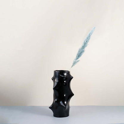 Modern black ceramic vase with artistic sculptural bumps styled in a minimal home decor setup on a wooden table with soft beige wall background.