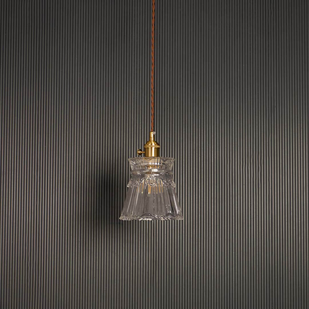 Unlit clear glass pendant light with brass top hanging on brown cord against black background for luxury home decor.