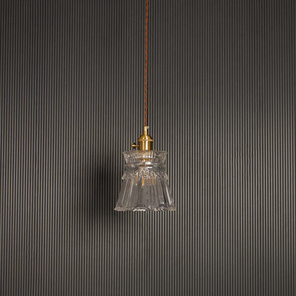 Unlit clear glass pendant light with brass top hanging on brown cord against black background for luxury home decor.
