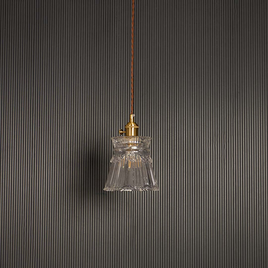 Unlit clear glass pendant light with brass top hanging on brown cord against black background for luxury home decor.