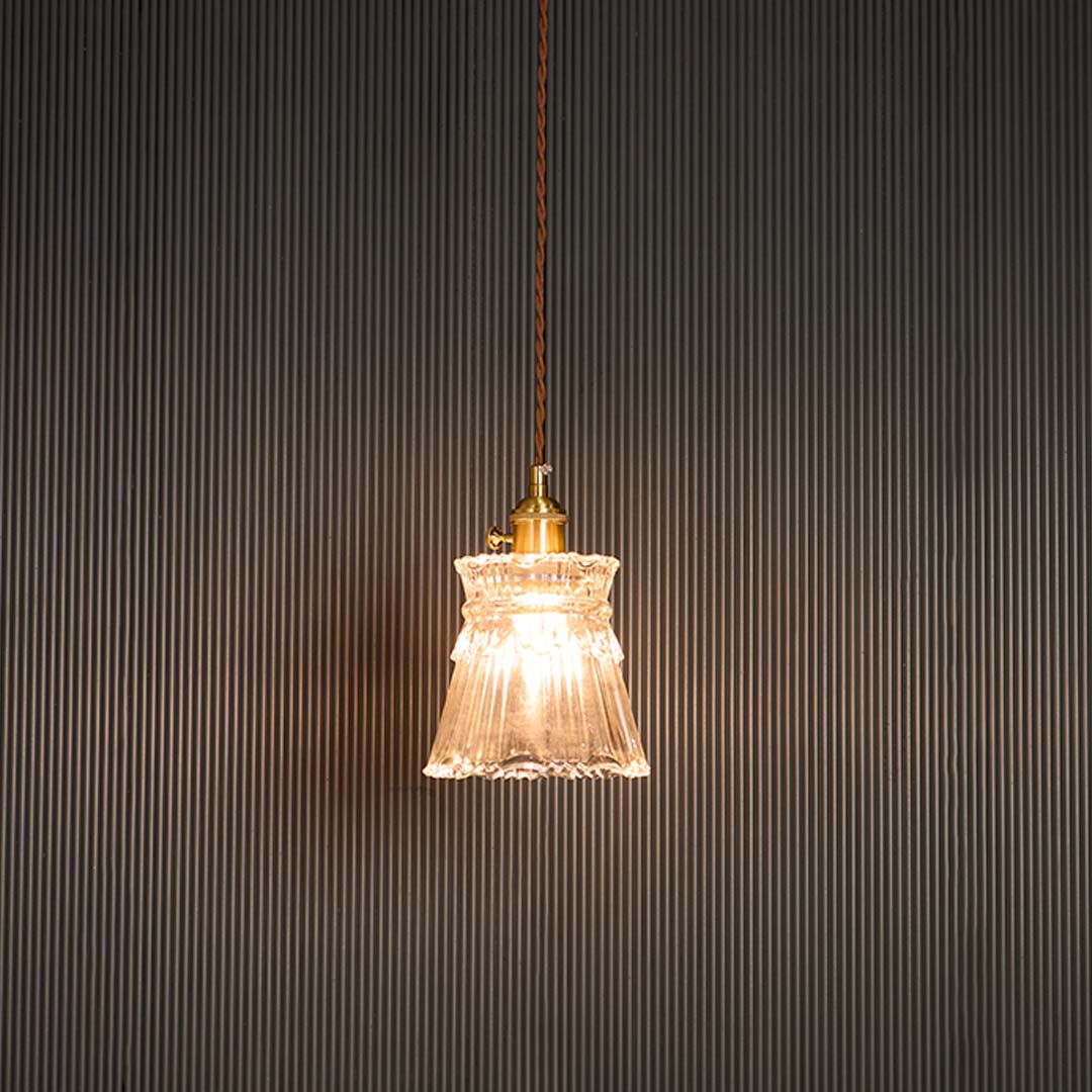 Clear glass pendant light glowing warmly with brass holder against black background for sophisticated room ambiance.
