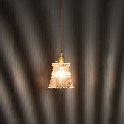 Clear glass pendant light glowing warmly with brass holder against black background for sophisticated room ambiance.