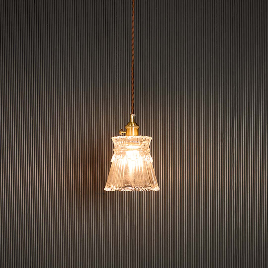 Clear glass pendant light glowing warmly with brass holder against black background for sophisticated room ambiance.