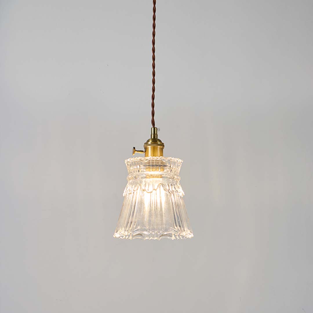 Clear fluted glass pendant light with brass holder glowing softly on white background for modern home interior decor.