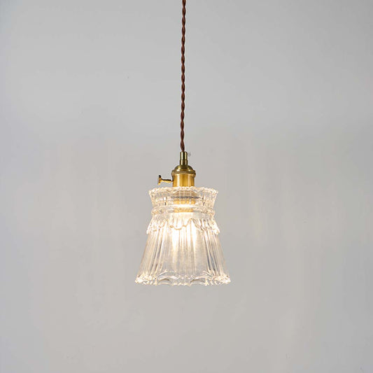 Clear fluted glass pendant light with brass holder glowing softly on white background for modern home interior decor.