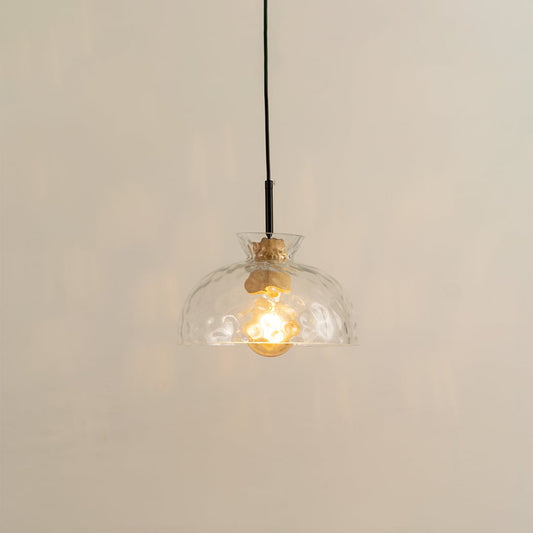 Clear dome glass pendant light with gold metal holder glowing softly on white background for modern home decor.
