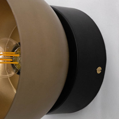 Close-up of black and gold metal wall light showing textured finish and clear bulb fixture.