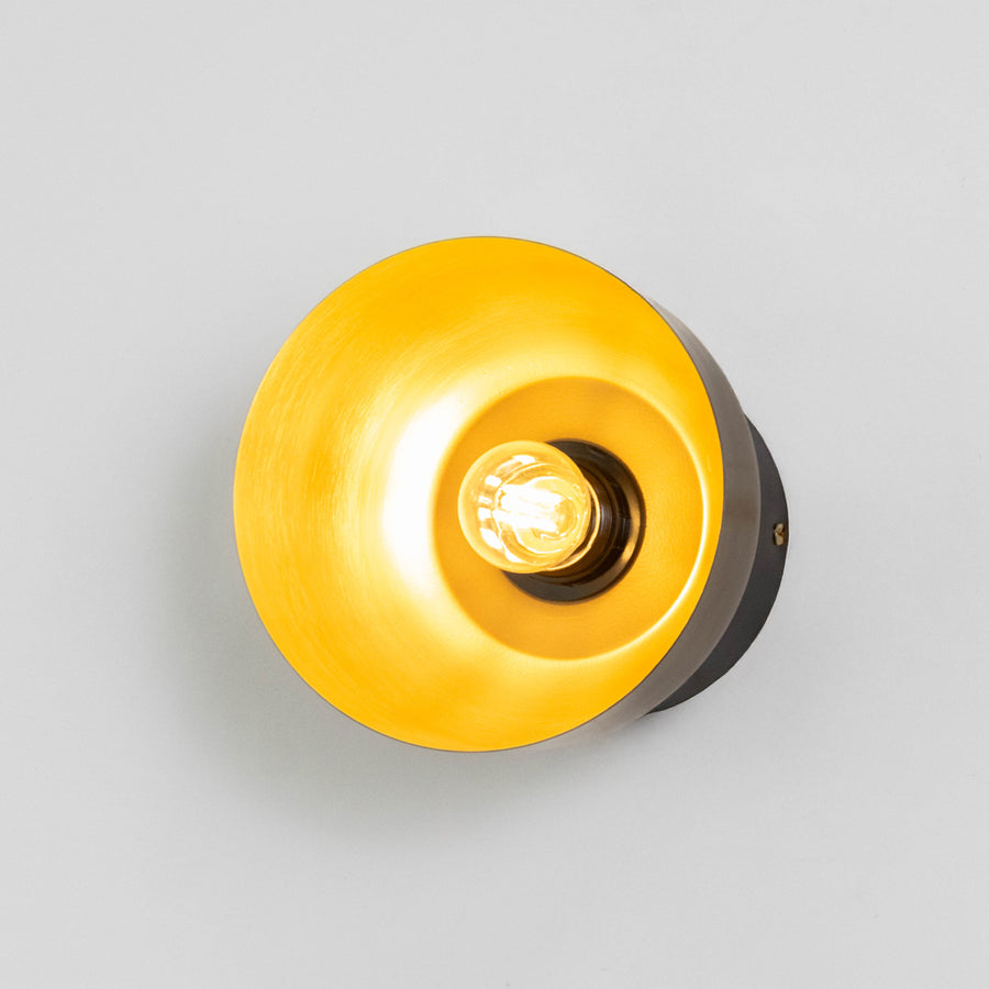 Contemporary wall light in gold metal finish with circular shade for bedroom or living decor lighting placement white background.