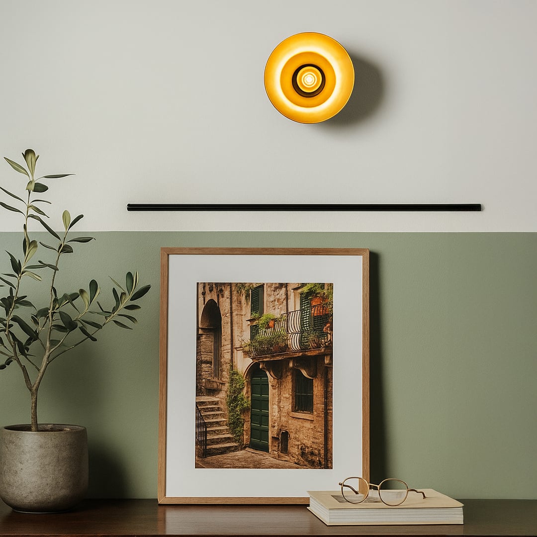 Warm oval wall light with gold interior mounted above framed art in modern hallway or entryway.