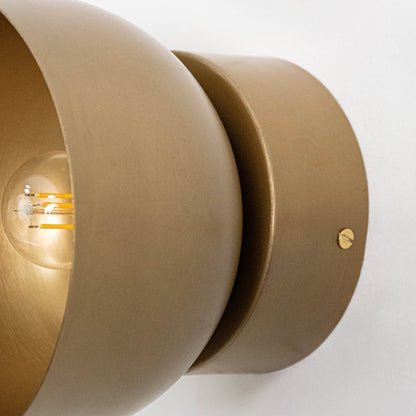 Detail of matte brass wall light fixture with smooth cylindrical shape and filament bulb inside.