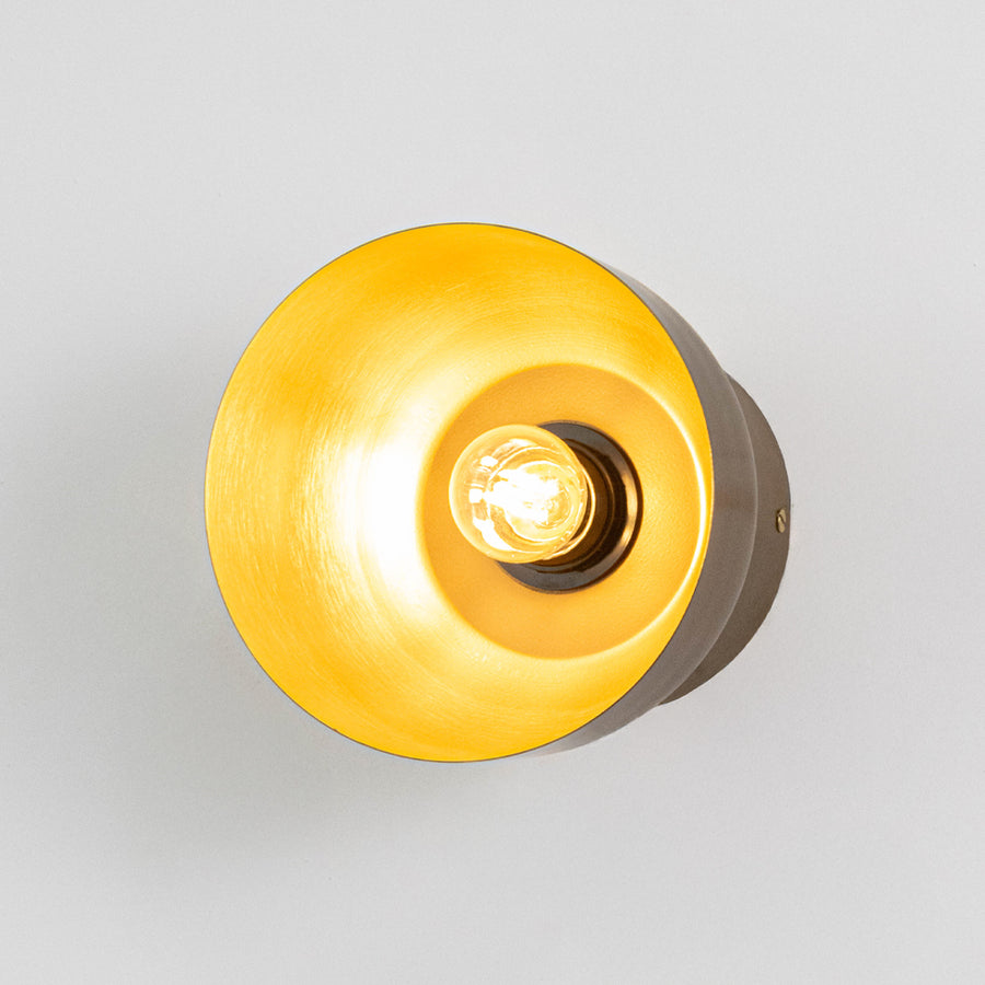 Modern wall light in gold metal finish with circular shade for bedroom or living room decor lighting white background.