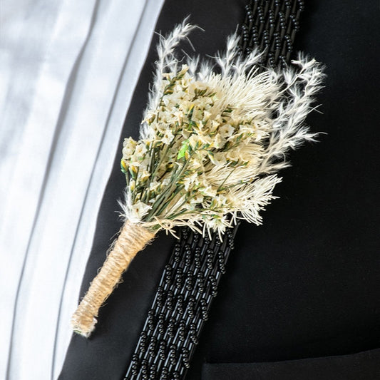 Closeup view of groom boutonniere with cream dried flowers and jute wrap pinned on black suit perfect for wedding decoration.