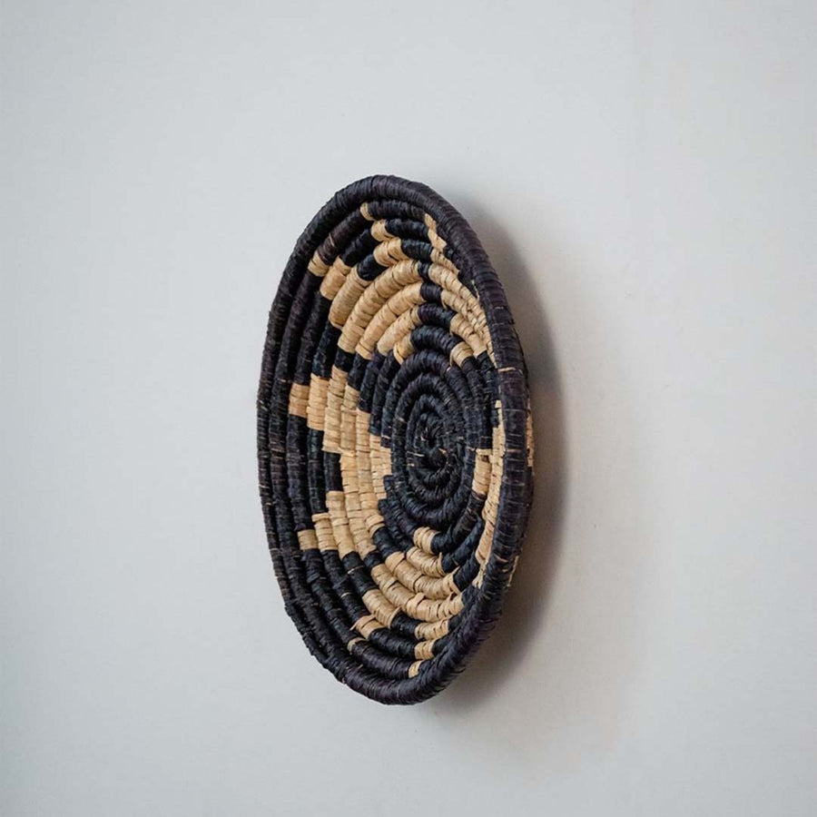 Eco friendly wicker wall decor basket in round shape with black and beige weaving for rustic living room wall styling.