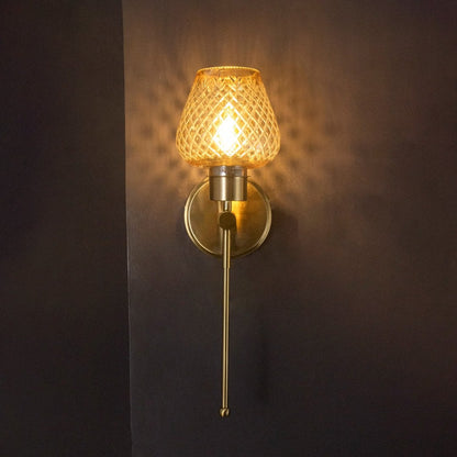 Glowing amber glass wall light with gold metal finish turned on suspended against a dark black background look.