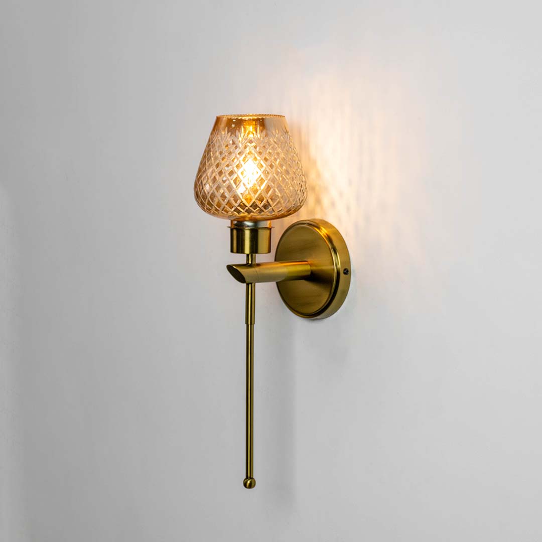 Illuminated gold wall sconce with textured amber glass shade glowing warmly against a clean white background view.