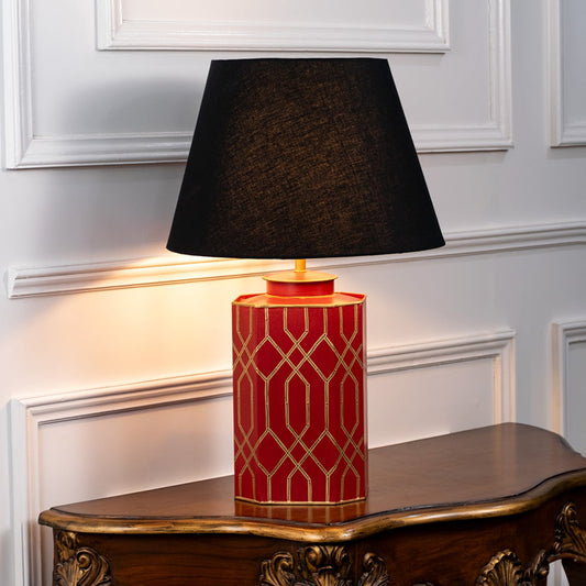 Table lamp on white background highlighting red ceramic base with gold geometric pattern topped with classic black shade.