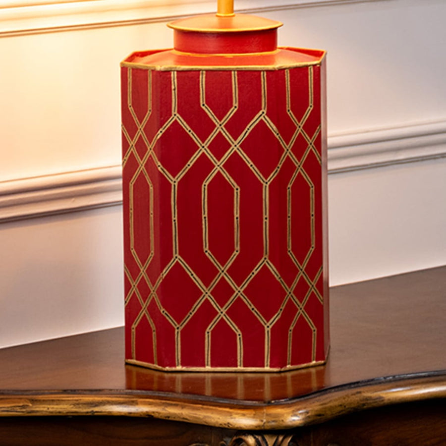Table lamp closeup highlighting red ceramic base with gold geometric design and smooth glossy surface.