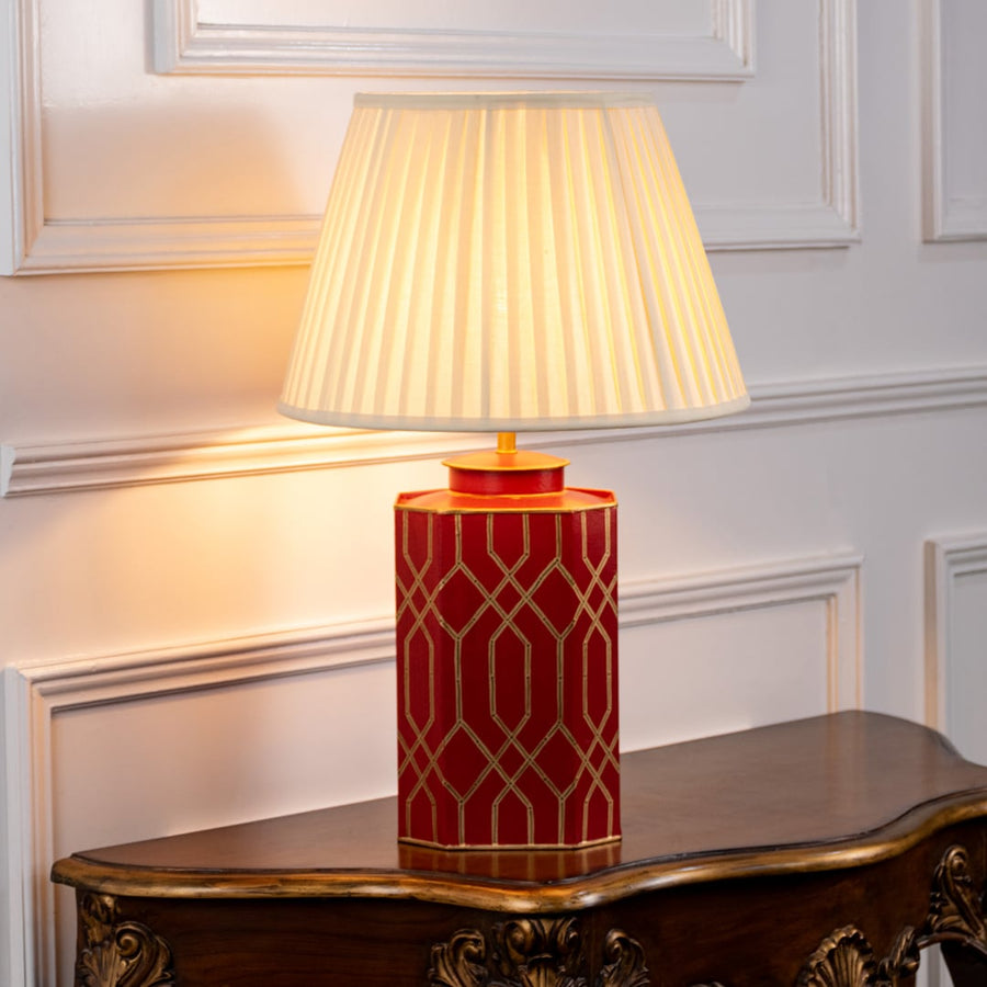 Elegant table lamp with pleated white shade and red ceramic base designed with geometric patterns and refined gold detailing.
