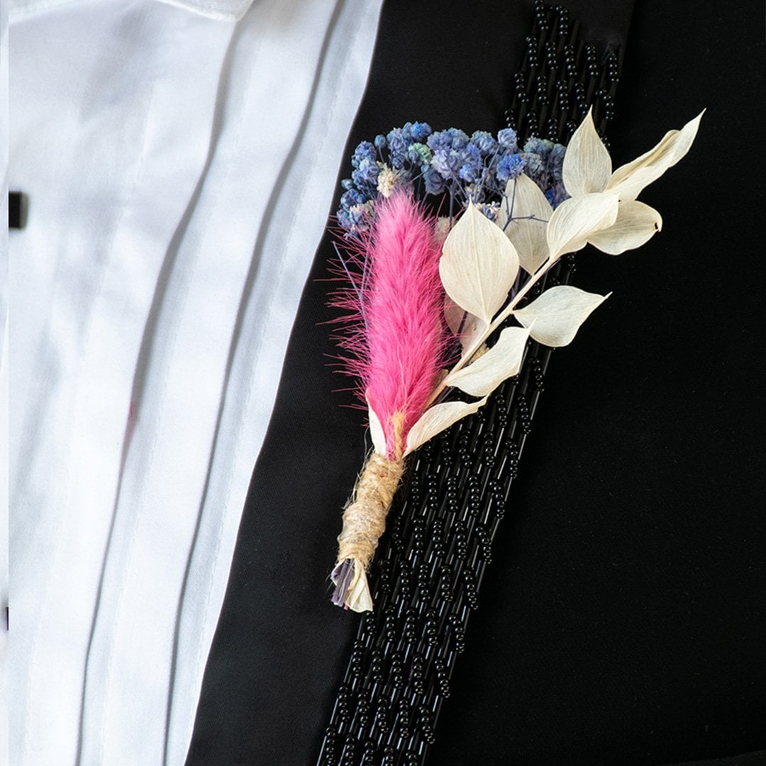 Closeup of dried boutonniere flower with pink stem blue preserved blooms and white leaves wrapped in jute creating an artificial wedding accessory.