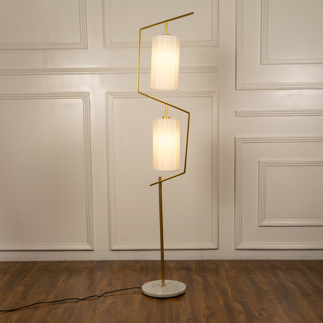 White floor lamp with geometric illuminated shades and brass stem creating elegant ambient lighting for modern spaces.