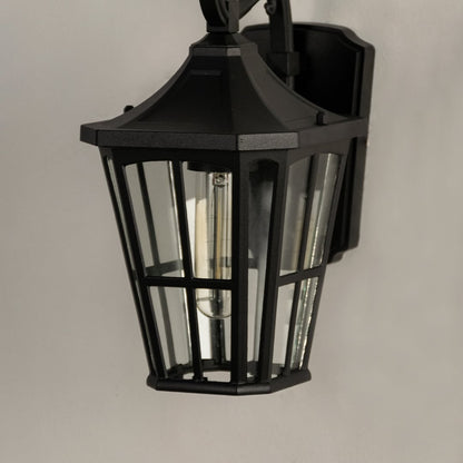 Closeup of black outdoor metal lantern with clear glass panels showing warm glowing bulb for elegant entrance and patio lighting.