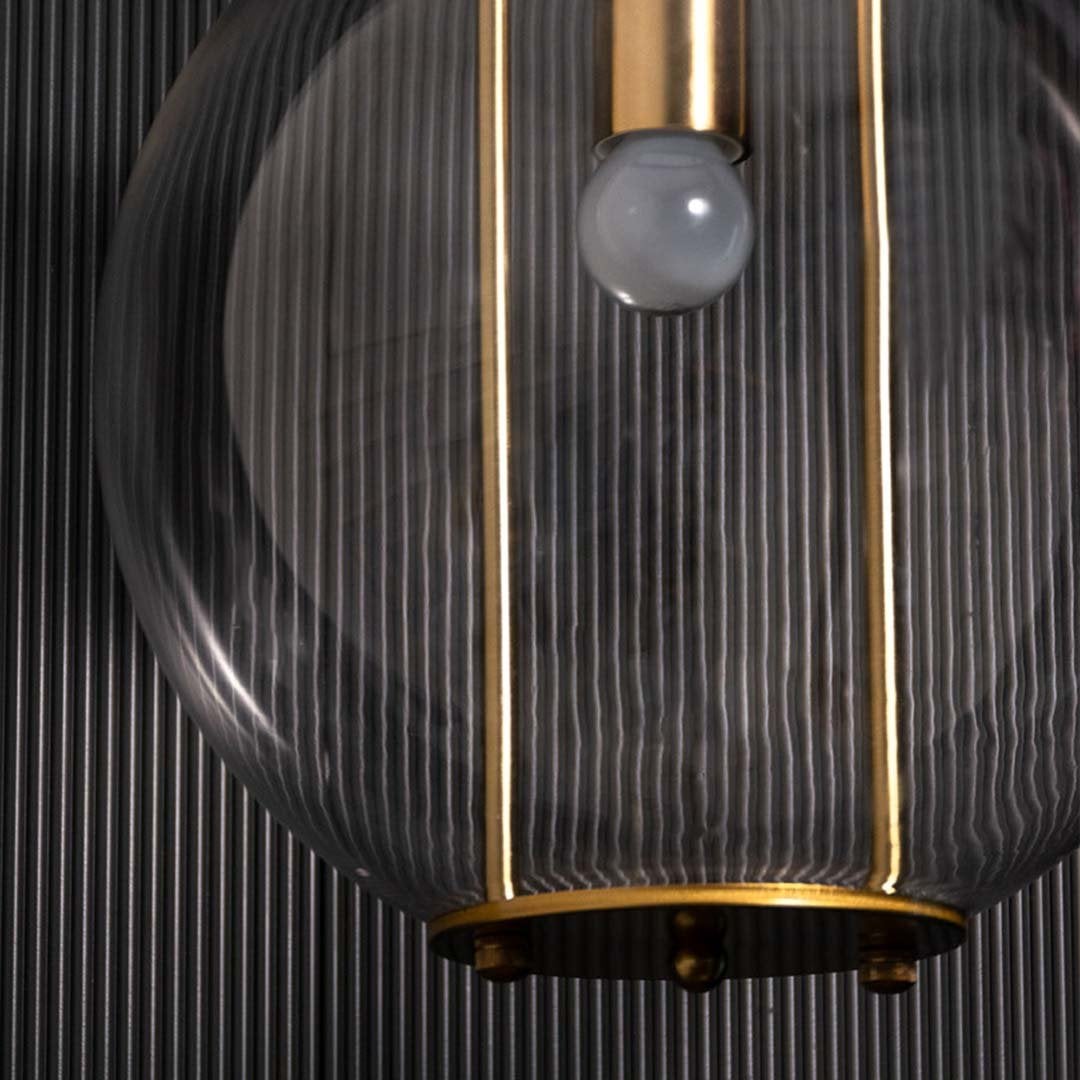 Detailed view of the pendant light showing the clear spherical glass shade gold metal rods and inner bulb holder with refined detailing.