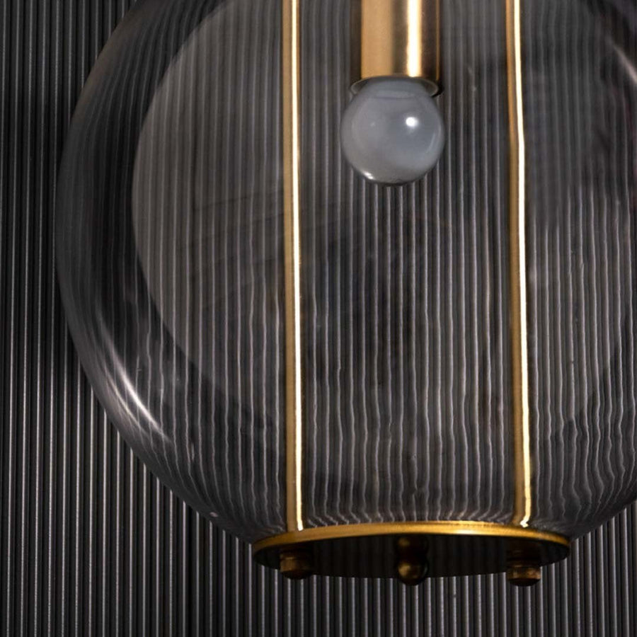 Detailed view of the pendant light showing the clear spherical glass shade gold metal rods and inner bulb holder with refined detailing.