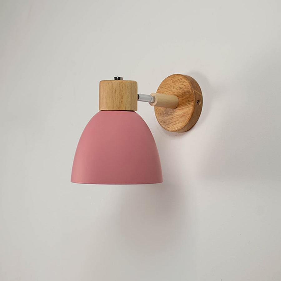Unlit matte pink metal wall sconce with natural wood details isolated on a clean white background showcasing its simple bell shape design.