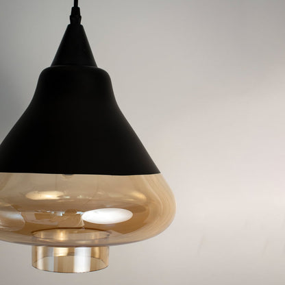 Amber glass pendant light with matte black top and transparent golden glass shade displayed with lights off.