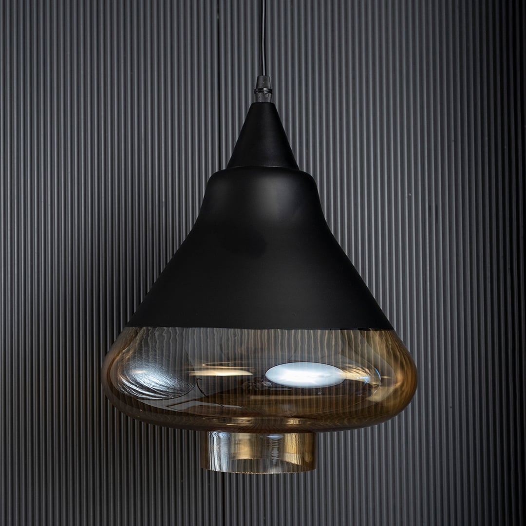 Amber glass pendant lamp turned off with smooth golden glass and black top shown against a black ribbed background.
