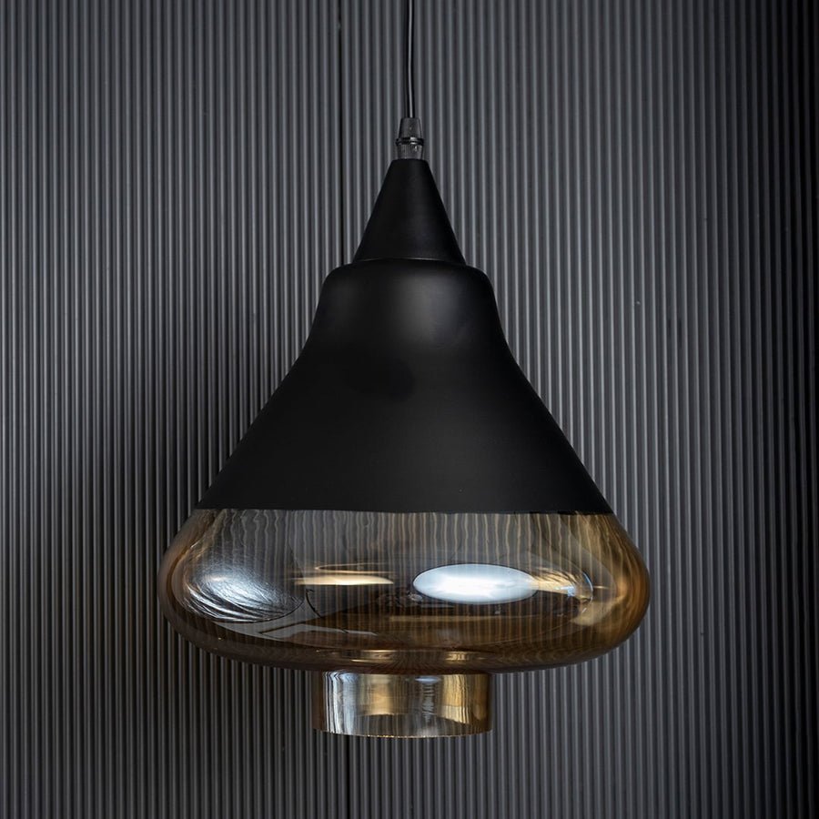 Amber glass pendant lamp turned off with smooth golden glass and black top shown against a black ribbed background.