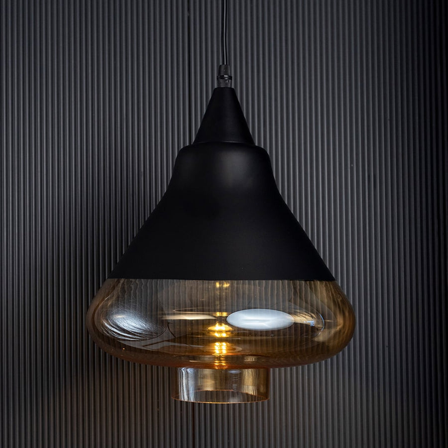 Amber glass pendant light turned off glowing through golden tinted glass against a dark ribbed background.