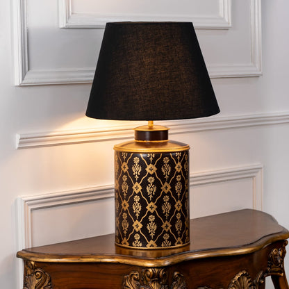 Table lamp on white background highlighting black and gold patterned ceramic base styled with a rich black fabric lampshade.