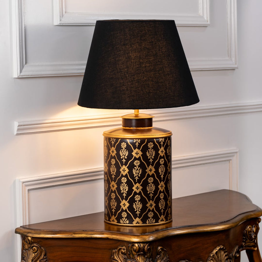 Table lamp on white background highlighting black and gold patterned ceramic base styled with a rich black fabric lampshade.