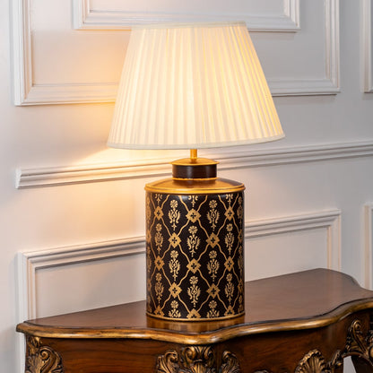 Table lamp on white background highlighting black and gold patterned ceramic base finished with a pleated fabric lampshade.