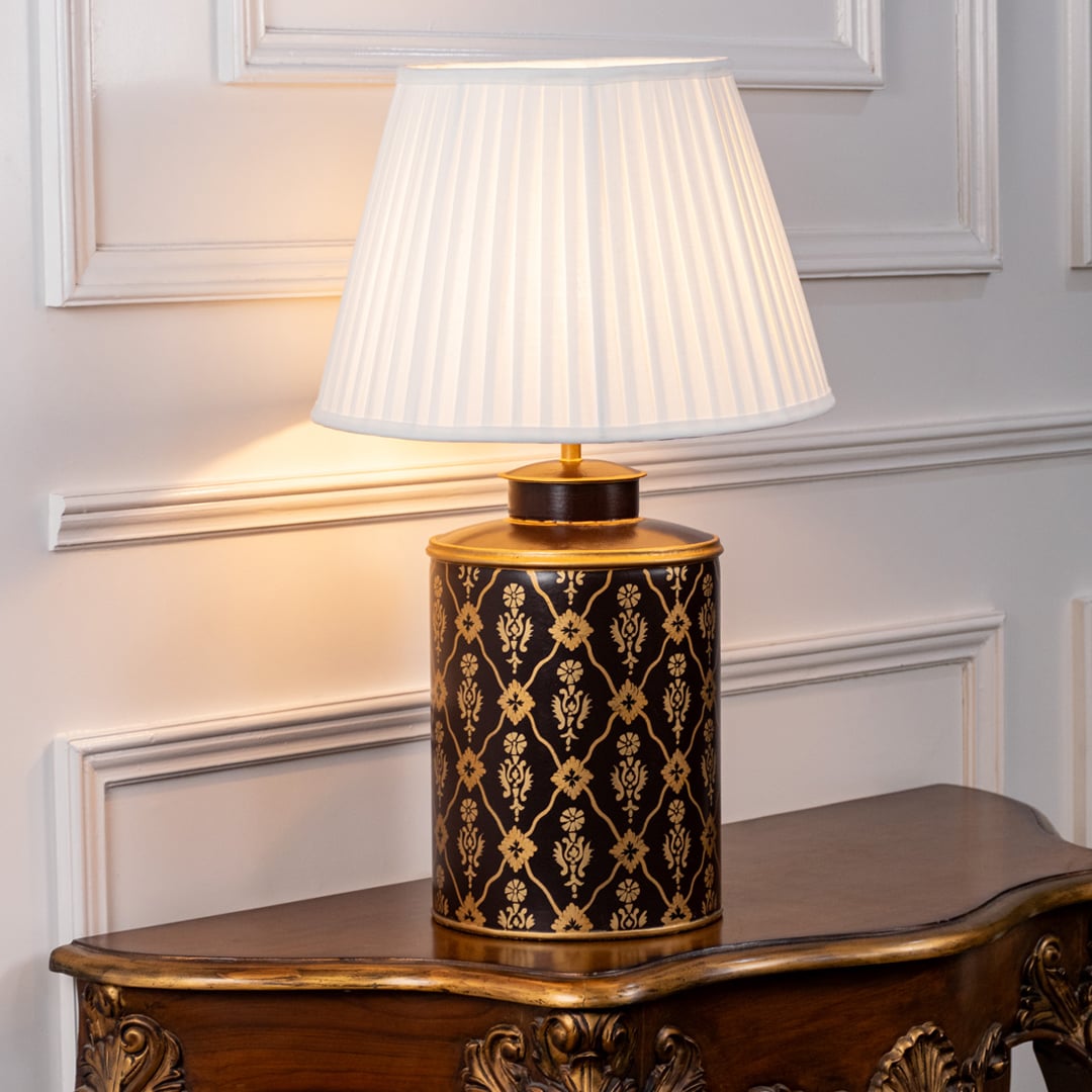 Table lamp on white background showcasing black and gold patterned ceramic base styled with a pleated fabric lampshade.