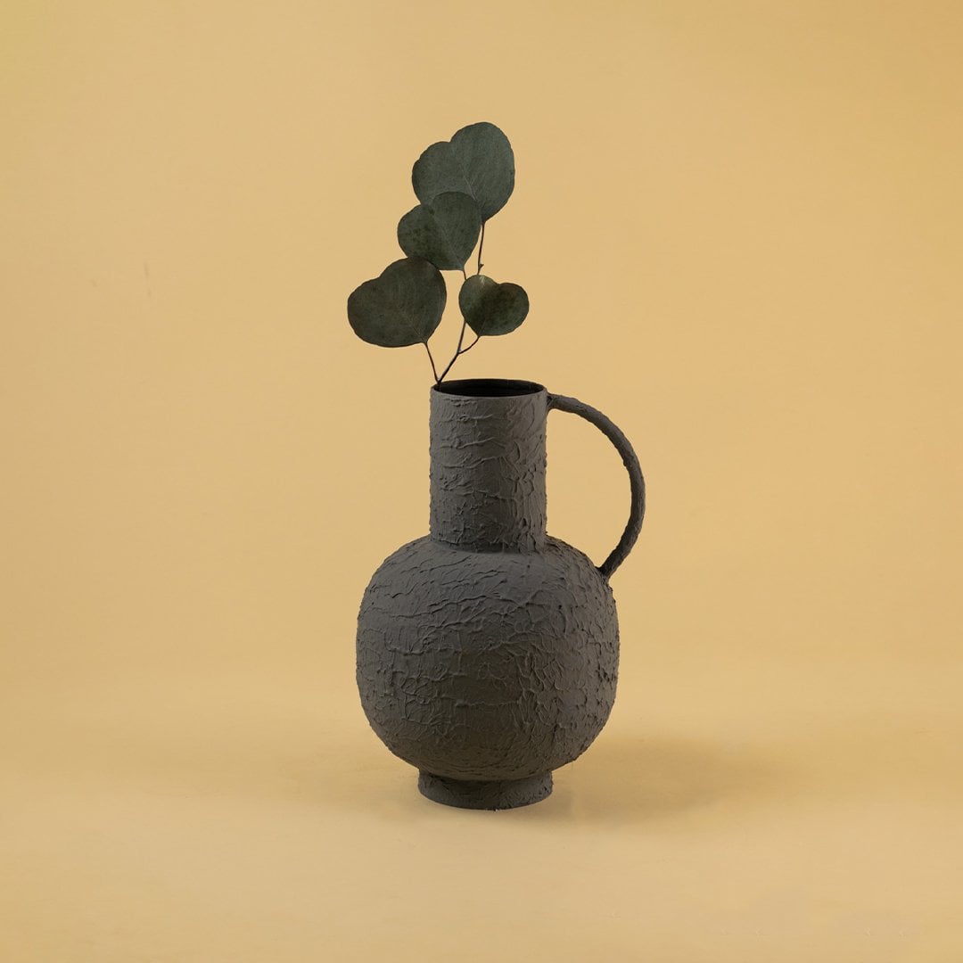 Styled interior with a grey textured jug vase displayed on a wooden coffee table beside neutral furnishings and soft lighting adding an elegant earthy decor touch.