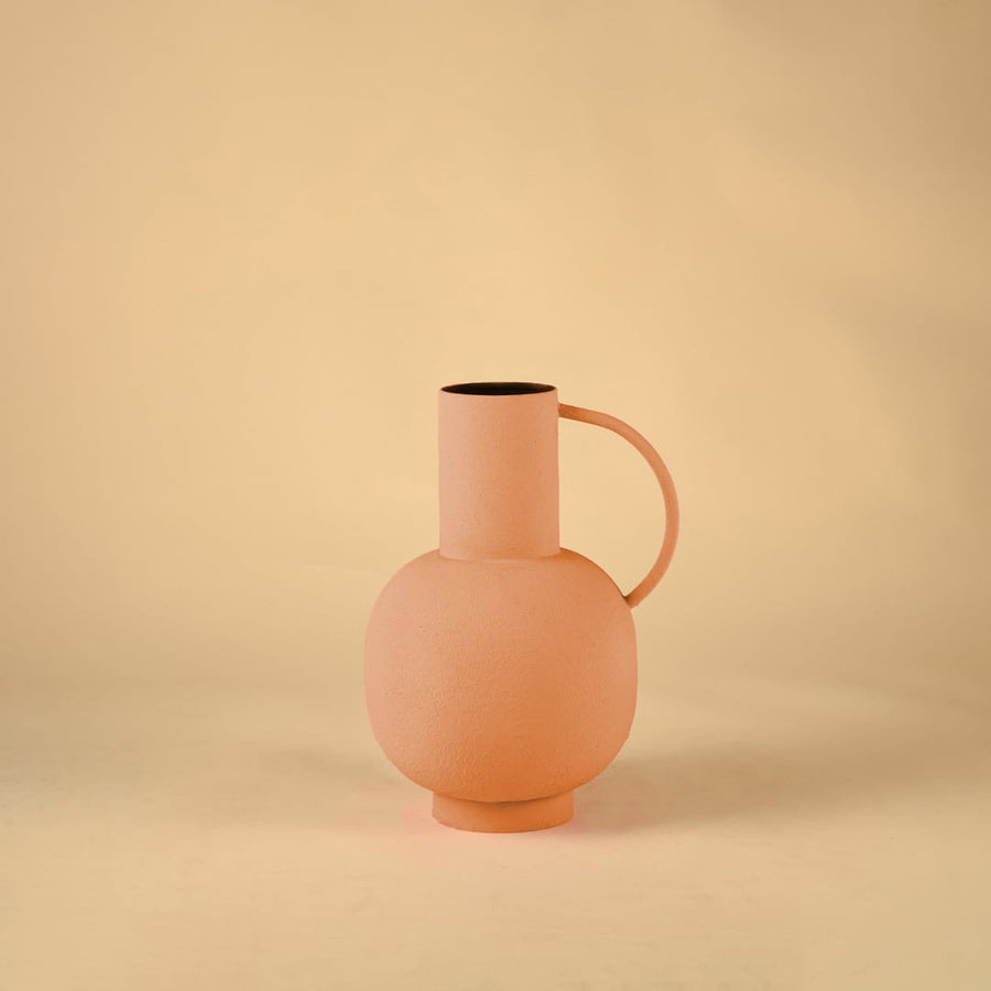 A peach ceramic style vase displayed on a plain white backdrop showcasing its simple rounded silhouette tall neck and curved handle for modern home styling.